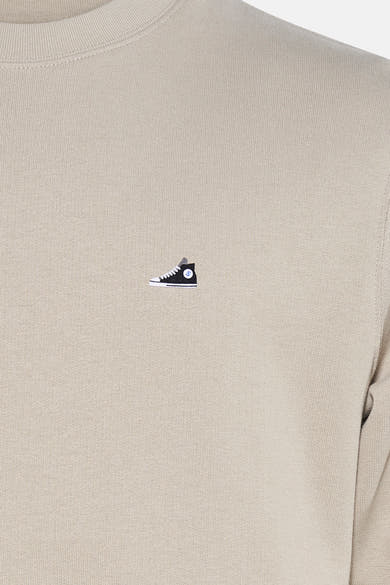 Beige sweater van STROM met een geborduurd motief van een hoge schoen op de voorkant.