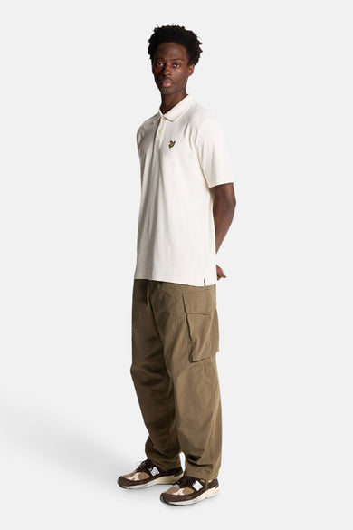 Polo beige à manches courtes de LYLE & SCOTT, porté avec un pantalon cargo marron et des baskets multicolores.