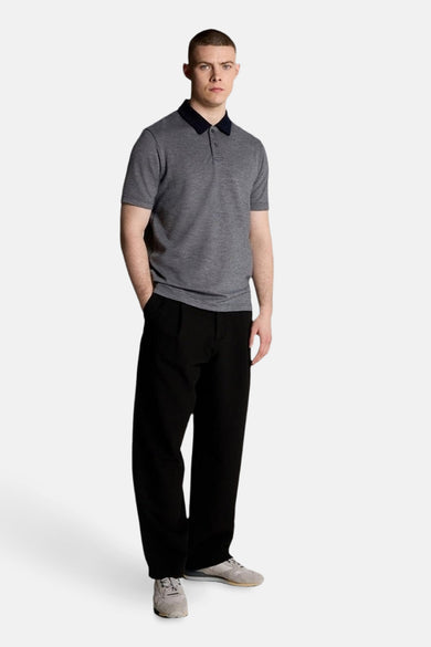 Blauw poloshirt met korte mouwen van LYLE & SCOTT, gedragen met een wijde zwarte broek en grijze sneakers.