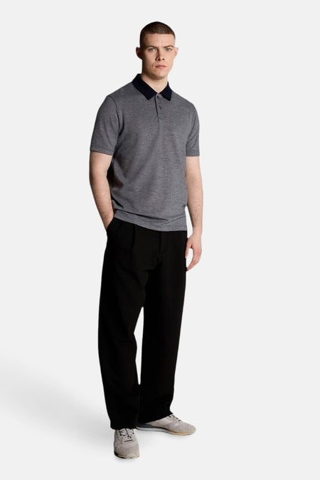 Blauw poloshirt met korte mouwen van LYLE & SCOTT, gedragen met een wijde zwarte broek en grijze sneakers.