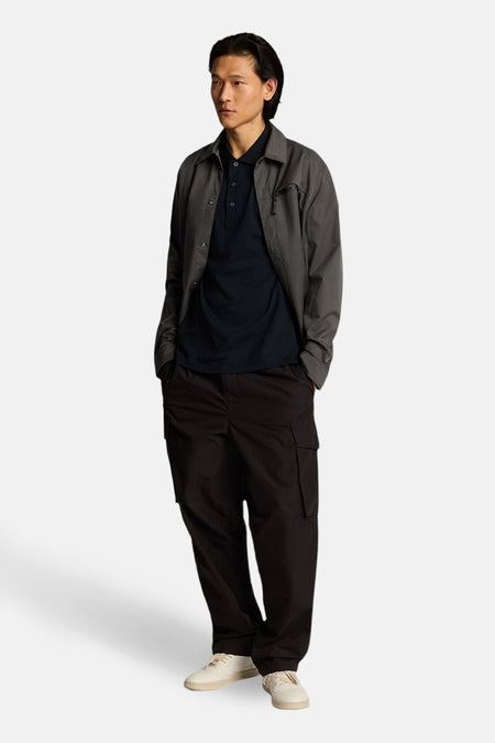 Marineblaues Kurzarm-Poloshirt von LYLE & SCOTT, getragen mit einer anthrazitgrauen Jacke und einer weiten schwarzen Cargohose.