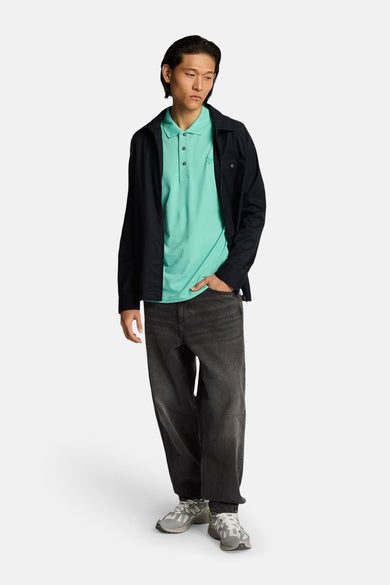 Turquoise poloshirt met korte mouwen van LYLE & SCOTT, gedragen met een open zwart overhemd en een wijde jeans.