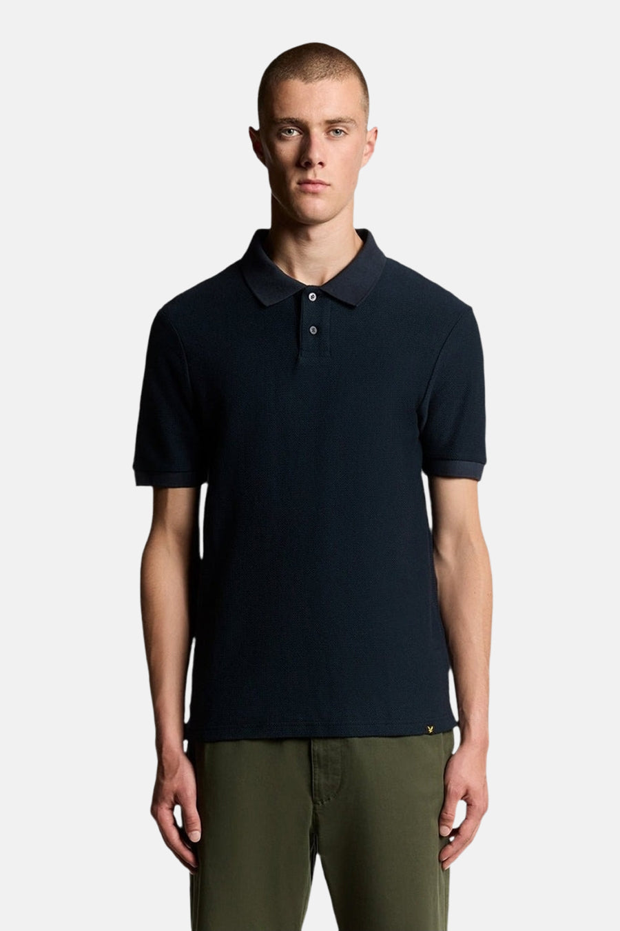 Polo bleu à manches courtes de LYLE & SCOTT, porté avec un pantalon kaki, sur fond blanc.