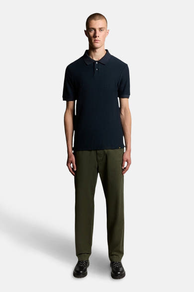 Polo bleu marine à manches courtes de Lyle & Scott, porté avec un pantalon vert olive et des chaussures noires à lacets.