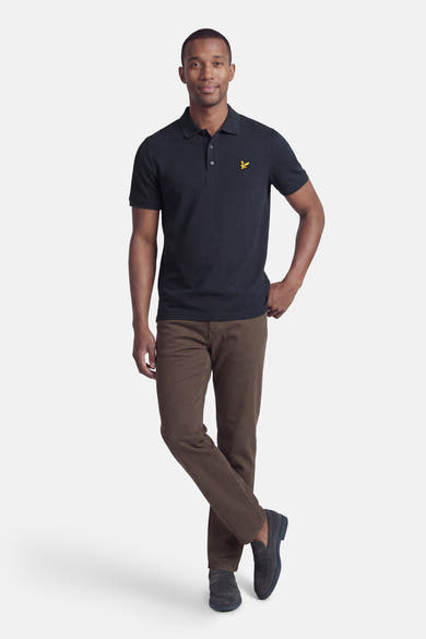 Polo bleu à manches courtes de Lyle & Scott, porté avec un pantalon marron et des mocassins, modèle masculin debout.