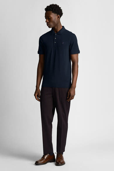Polo bleu marine à manches courtes par LYLE & SCOTT, porté avec un pantalon rayé marron et des chaussures habillées.