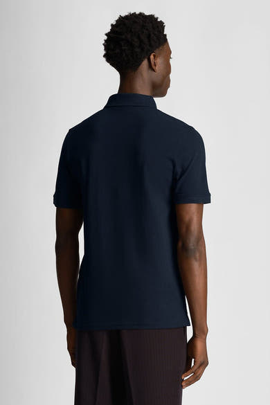 Polo à manches courtes bleu de LYLE & SCOTT, vue de dos, porté avec un pantalon marron rayé.