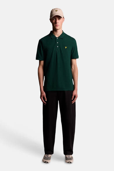 Groen poloshirt van LYLE & SCOTT met klassieke kraag, witte knopen en geel adelaarslogo, gedragen door een man met een beige pet.