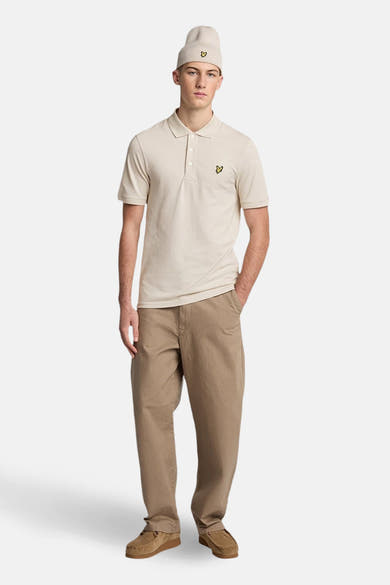 Polo à manches courtes beige de Lyle & Scott, porté avec un bonnet et un pantalon décontracté marron clair.