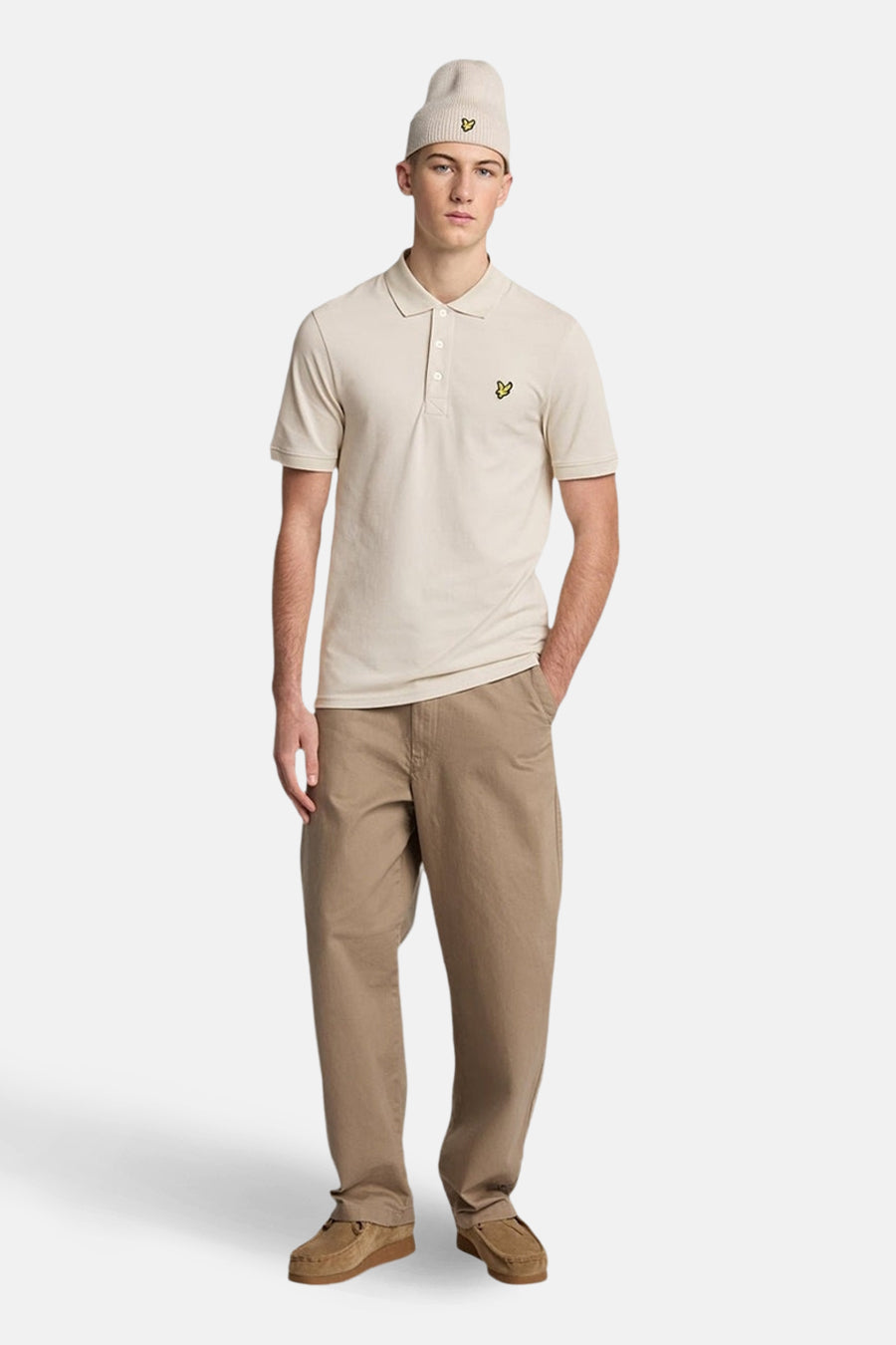 Polo à manches courtes beige de Lyle & Scott, porté avec un bonnet et un pantalon décontracté marron clair.