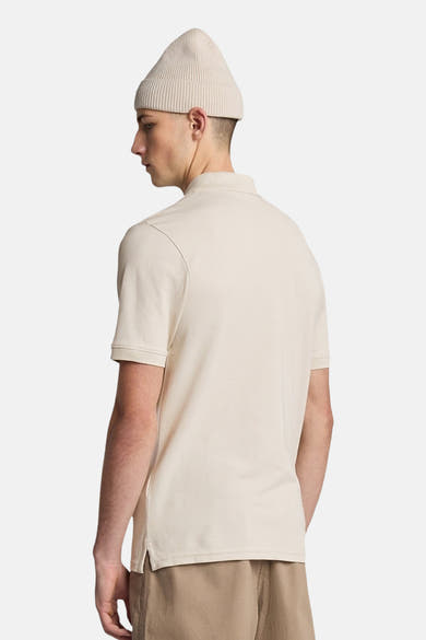 Polo beige à manches courtes de LYLE & SCOTT, porté avec un bonnet couleur crème et un short beige.