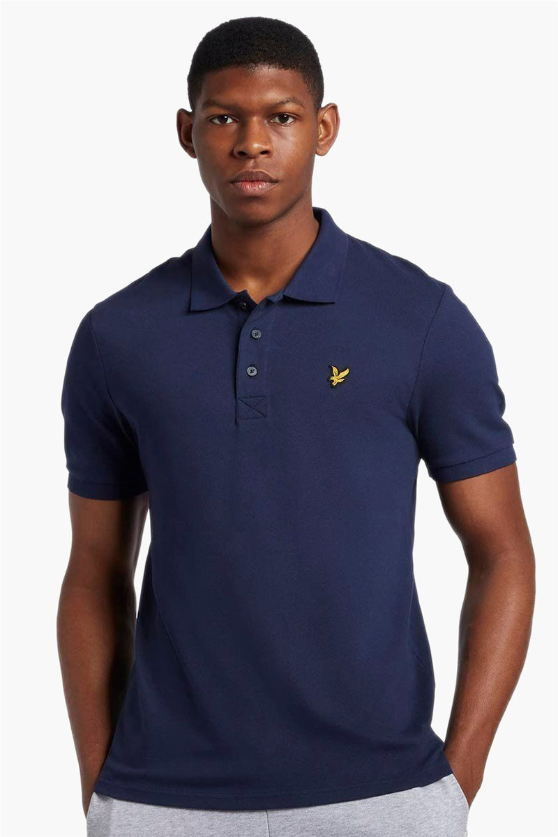 Navy blue short-sleeve polo shirt by Lyle & Scott, featuring yellow embroidered bird logo on chest, classic collar, and button placket, front view on model.