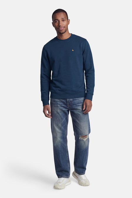 Blauwe rondehals sweatshirt van STROM met een klein oranje zeilbootmotief op de borst.