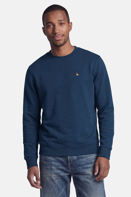 Rondehals sweatshirt STROM blauw met klein oranje en roze geborduurd logo op de borst, gedragen door een man.