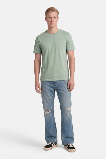 Groen STROM T-shirt met een klein geel geborduurd motief op de borst, gedragen door een man.