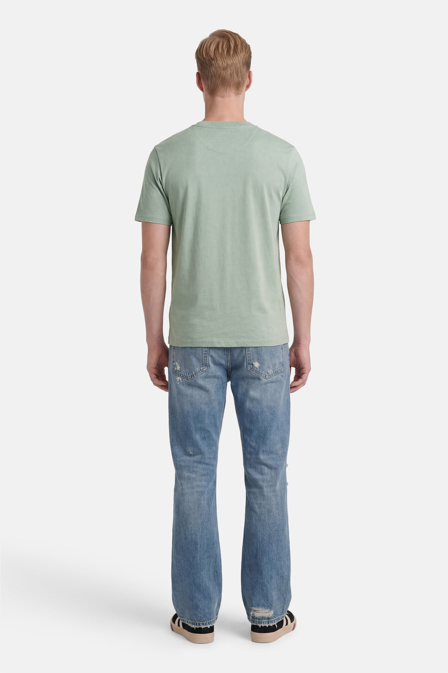 Lichtgroen T-shirt van STROM met ronde hals, achterkant, gedragen met een verbleekte spijkerbroek en sneakers.