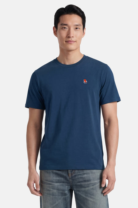 Blauw T-shirt met korte mouwen van STROM, met een klein rood-wit stoellogo geborduurd op de borst, gedragen met een spijkerbroek.