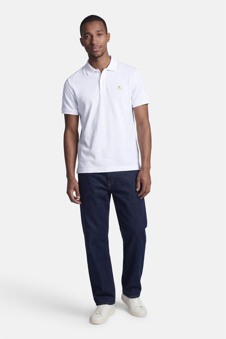 Witte STROM polo, versierd met een geborduurd spaghettimotief op de borst, gedragen door een man met een donkere spijkerbroek en witte sneakers.