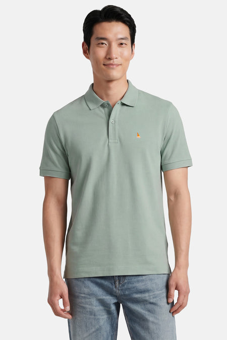 Groen STROM poloshirt met klein oranje en roze patroon, gedragen door een man in een blauwe spijkerbroek.