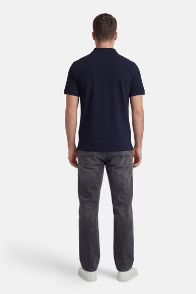Marineblauwe polo van STROM, in pique gebreid, van achteren gedragen met een grijze jeans en witte sneakers.