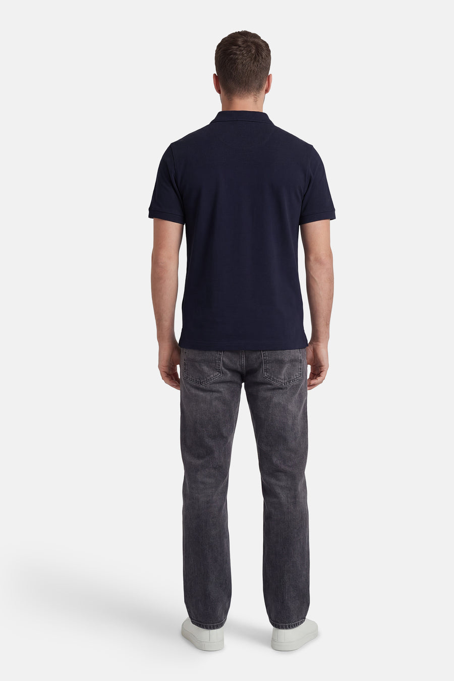 Marineblauwe polo van STROM, in pique gebreid, van achteren gedragen met een grijze jeans en witte sneakers.