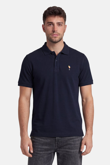 Marineblauwe polo van STROM met cocktailglasborduurwerk, kraag met twee knopen, gedragen met een grijze jeans.