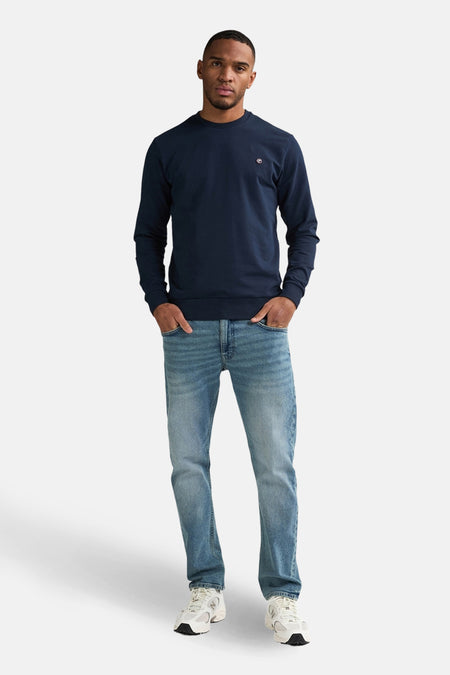 Jean droit bleu clair de Petrol Industries, porté avec un pull bleu marine et des baskets blanches.
