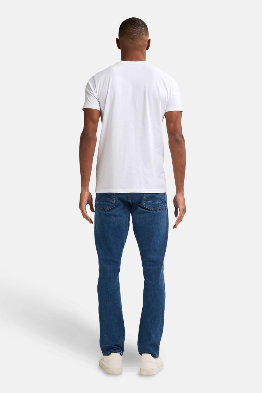 Jean droit bleu moyen de Petrol Industries®, vue de dos, porté avec un t-shirt blanc et des chaussures de sport.
