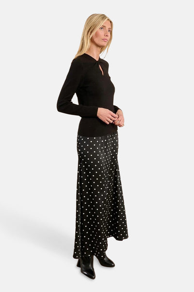Pull à col rond noir de Molly Bracken, porté avec une longue jupe noire à pois blancs et des bottines noires pointues.
