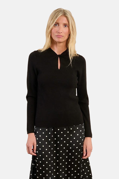 Pull à col rond noir par Molly Bracken avec une ouverture en forme de goutte d'eau, porté sur une jupe à pois.