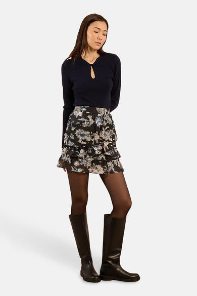 Ronde hals trui blauw van Molly Bracken met een druppelvormige opening bij de hals, gedragen met een rok met ruches en een print en zwarte laarzen.