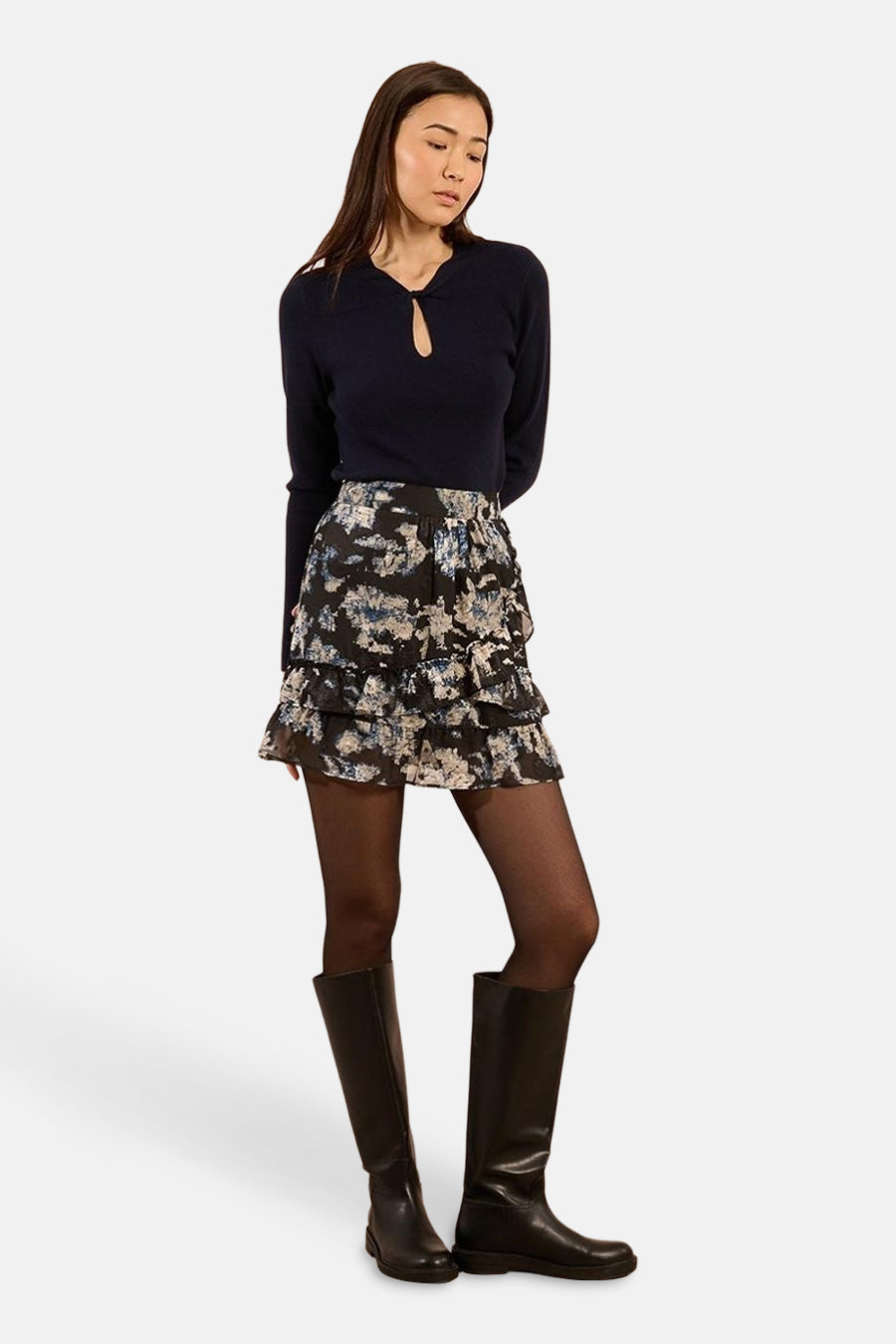 Ronde hals trui blauw van Molly Bracken met een druppelvormige opening bij de hals, gedragen met een rok met ruches en een print en zwarte laarzen.