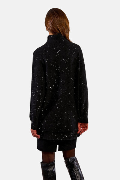 Zwarte jurk met lange mouwen van Molly Bracken, bezaaid met decoratieve stippen, gedragen met zwarte laarzen.
