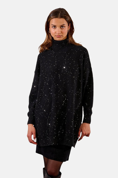 Zwarte jurk met lange mouwen van Molly Bracken, bezaaid met glinsterende pailletten, gedragen met een zwarte panty en laarzen.
