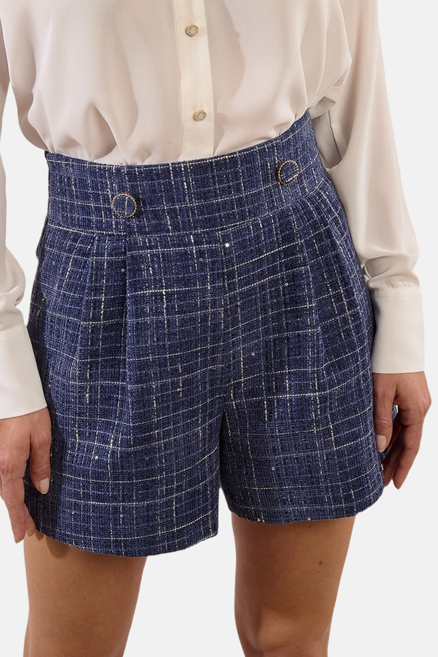 Korte blauwe geruite short van Molly Bracken, van achteren gezien, gedragen met een blouse en rode lakleren enkellaarsjes.