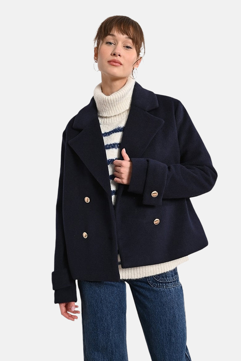 Korte blauwe jas van Molly Bracken met dubbele gouden knoopsluiting, gedragen over een gestreepte trui en een spijkerbroek.