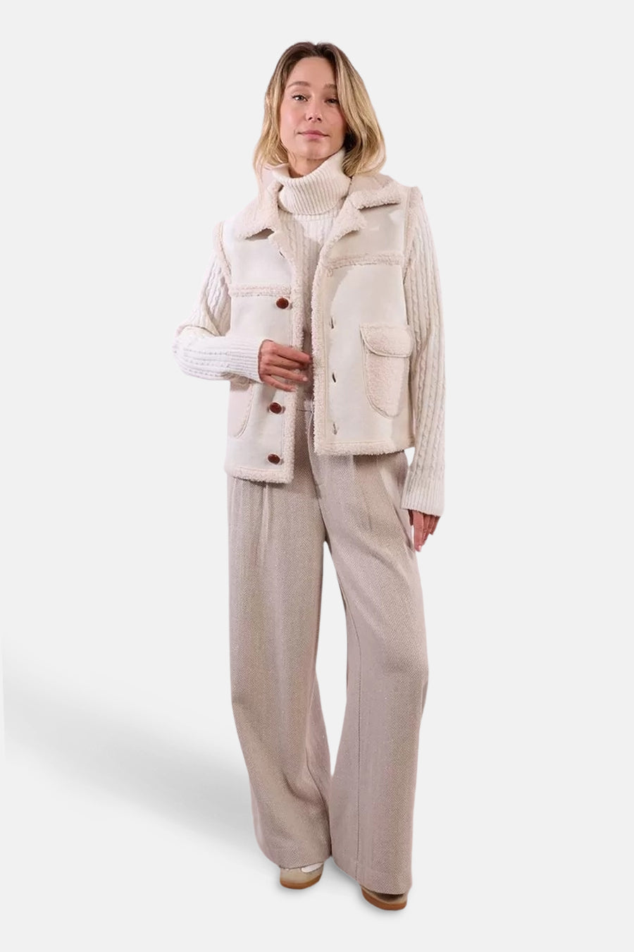 Beige mouwloos vest van Molly Bracken met bruine knopen, gedragen over een kabelgebreide trui.