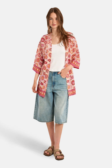 Multikleurend vest van Molly Bracken met bloemenpatroon gedragen over een witte tanktop en een spijkerbroek met korte pijpen.