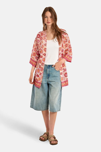 Multikleurend vest van Molly Bracken met bloemenpatroon gedragen over een witte tanktop en een spijkerbroek met korte pijpen.