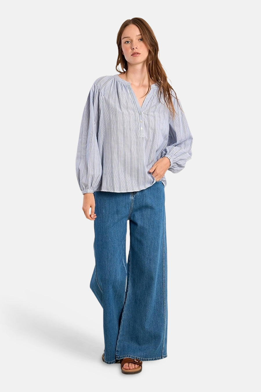 Chemisier à manches longues bleu rayé by Molly Bracken, porté avec un jean large et des sandales marron.