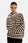 Multicolored striped turtleneck sweater with soft textured knit, worn by model in front view, paired with black pants