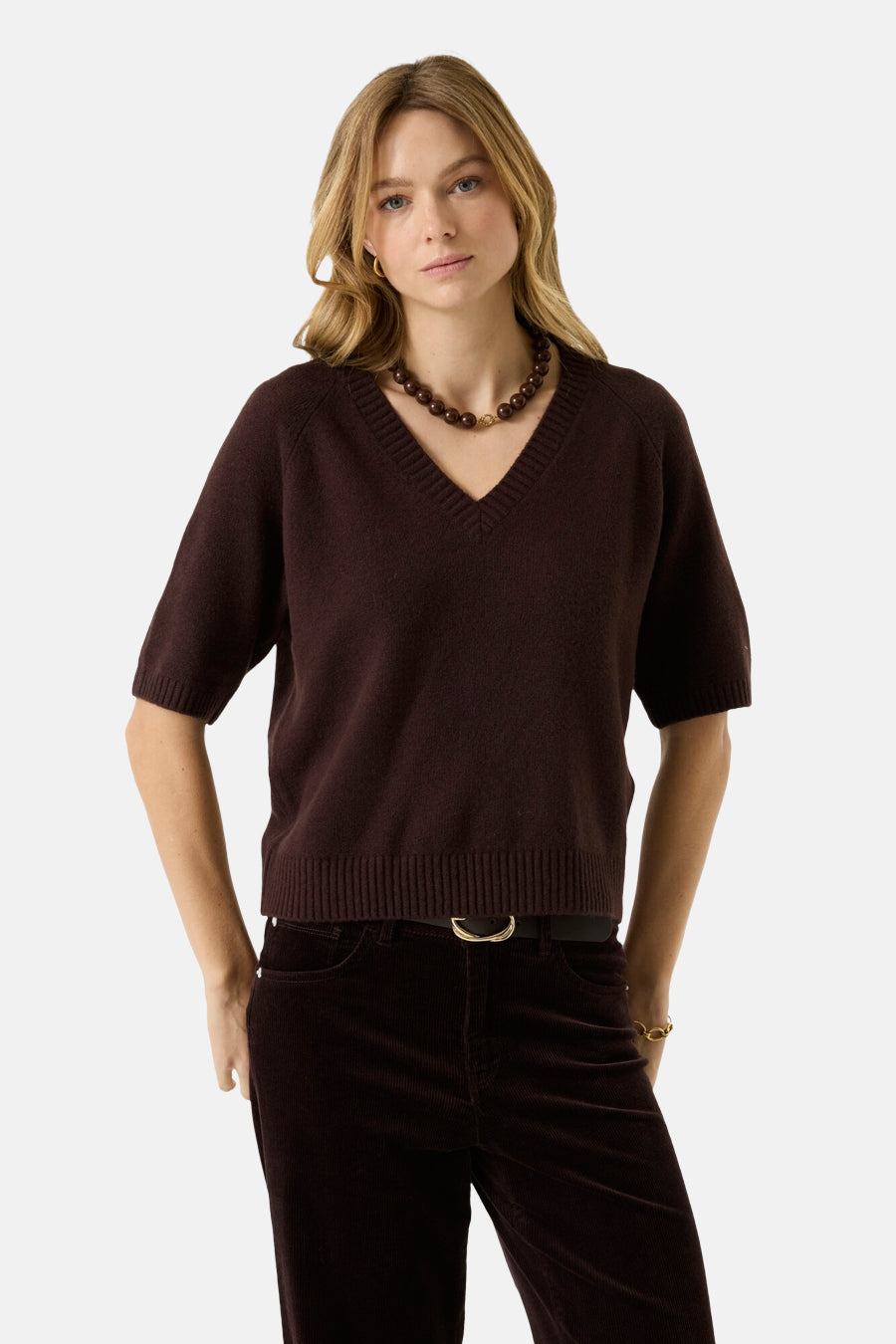 Brown V-neck short-sleeve knit sweater with ribbed hem and cuffs, worn with dark corduroy pants and beaded necklace, front view.