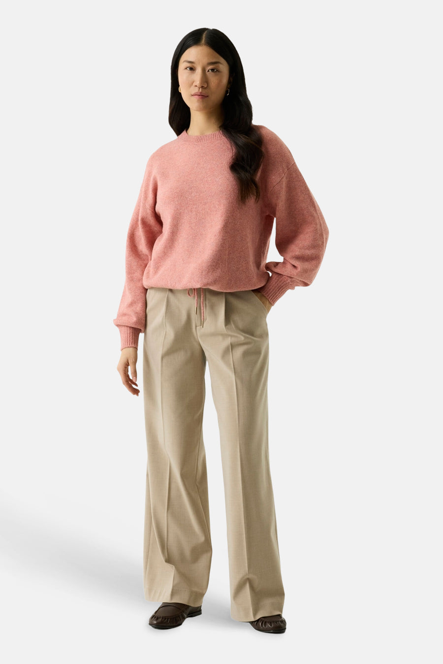 Coral crewneck sweater with soft textured knit, relaxed fit, and ribbed cuffs, worn with beige wide-leg trousers and brown loafers, full-length front view