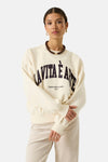 Ecru crewneck sweatshirt with bold black arched text "LA VITA È ARTE" and smaller slogan, worn by model with arms crossed, paired with matching ribbed pants.