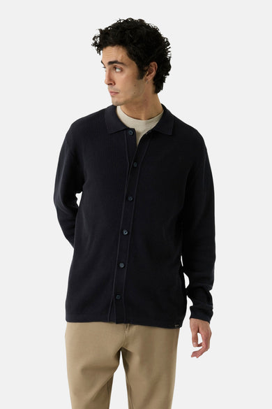 Navy ribbed knit gilet with button front and collar, worn over a beige crewneck, side view on model.