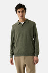 Olive green ribbed-knit turtleneck sweater with buttoned collar, worn by model in front view, paired with beige trousers