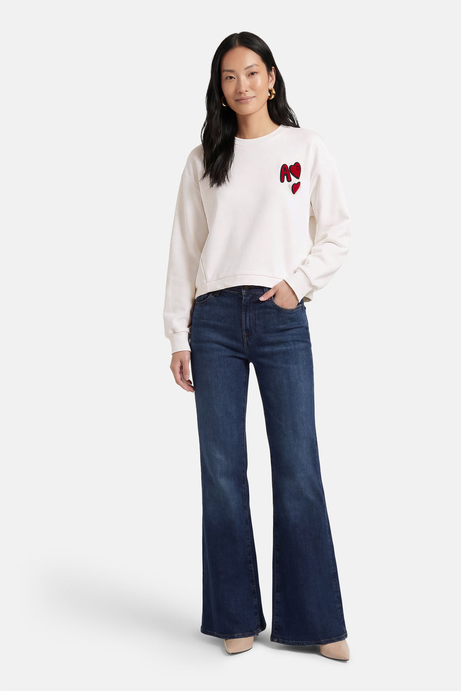 Sweat col O blanc d'ADORE, avec des motifs rouges en forme de cœur et porté avec un jean évasé.
