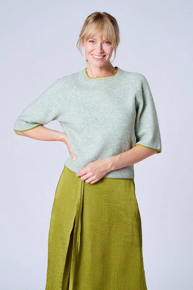 Pull vert clair en laine de TERRE BLEUE, avec des bords contrastés et porté avec une jupe vert olive.