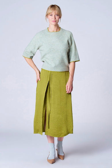 Pull vert de TERRE BLEUE avec bordure jaune, porté avec une jupe verte et des chaussures à talons.