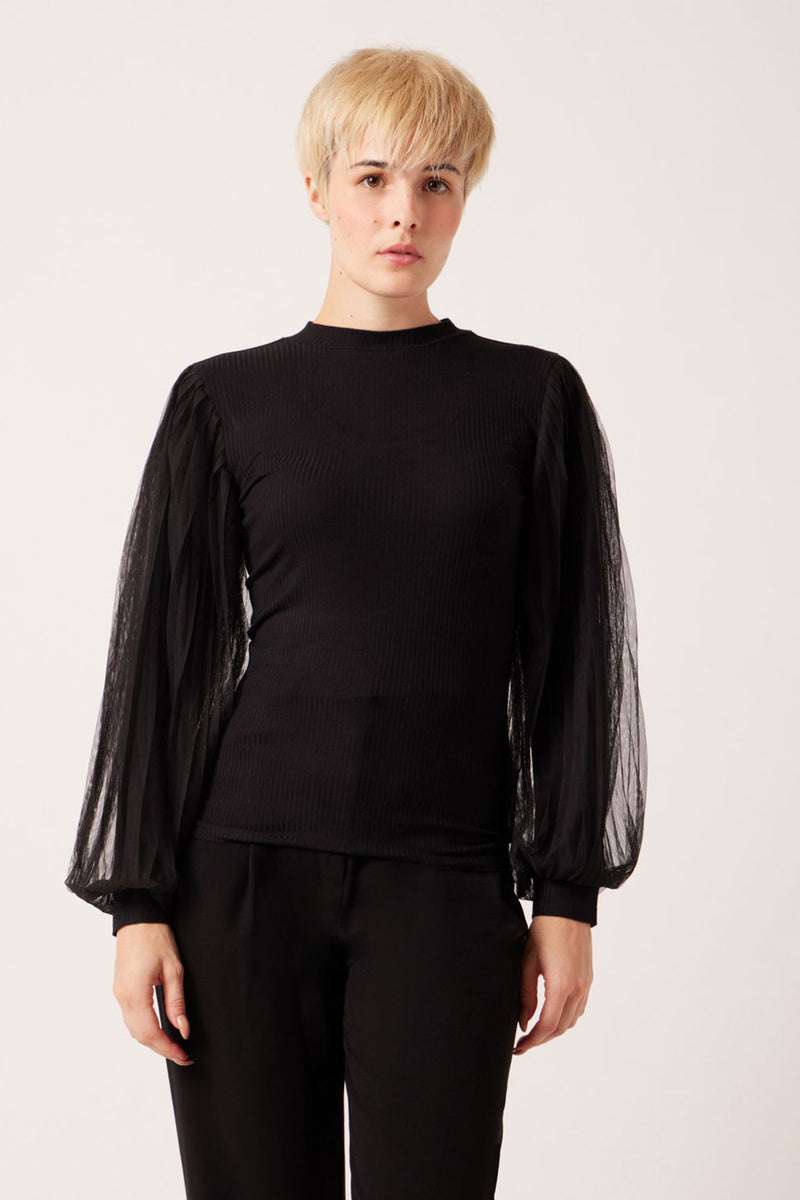 Black ribbed long-sleeve top with sheer puffed sleeves, front view, model wearing black pants